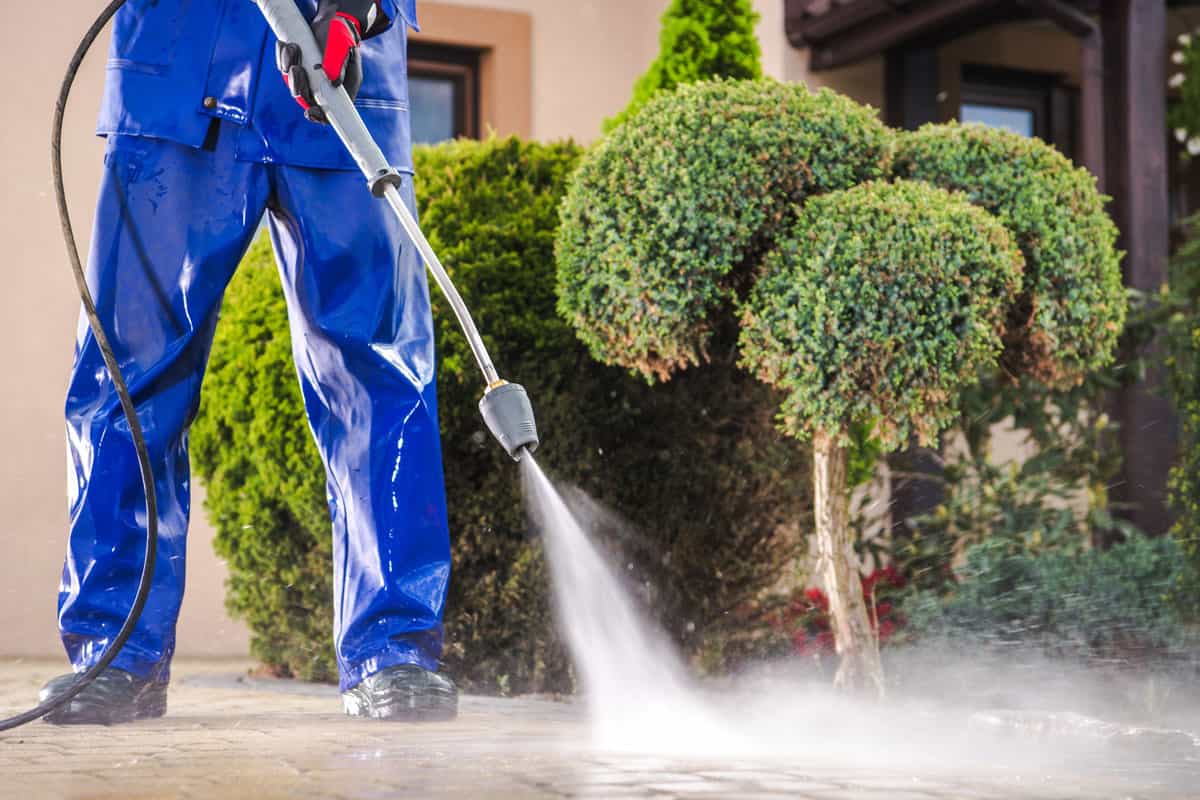 Caucasian Worker in His 30s with Pressure Washer Cleaning Residential Driveway