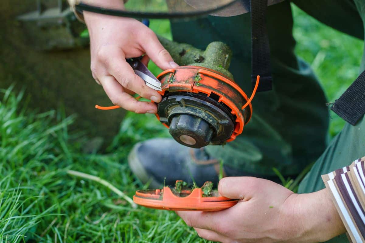 Close up on string trimmer head unknown caucasian man holding and repairing weed cutter replacing parts replacement in day on the field farmer or gardener. 