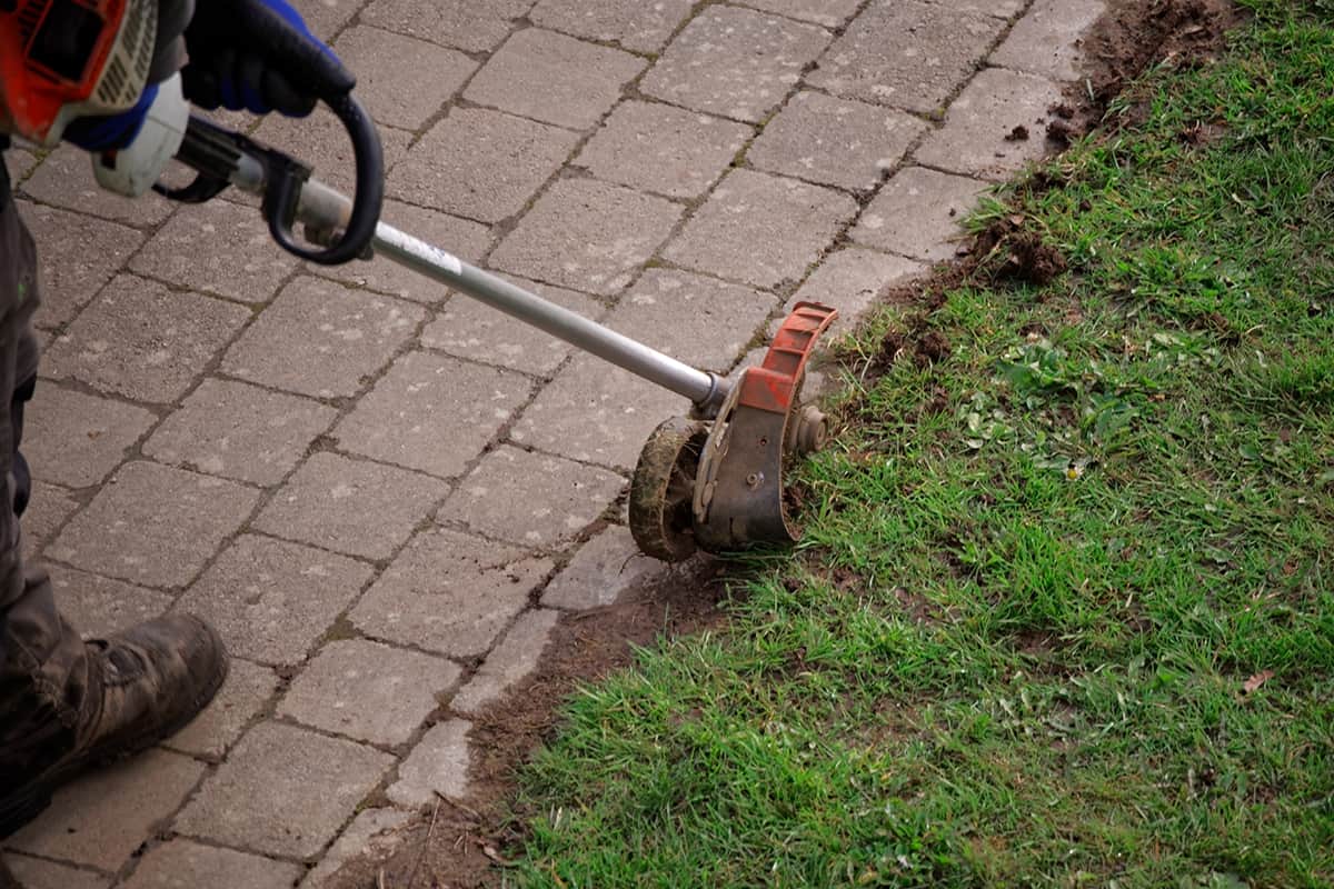 Garden maintenance worker uses an edge trimmer at the pathway