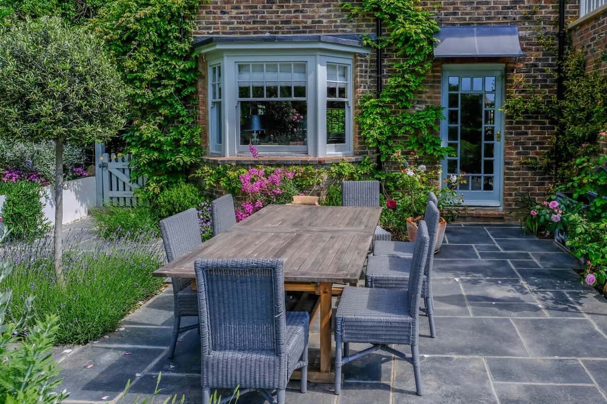 Large table and chairs on slate patio with Mediterranean plants in a back garden 