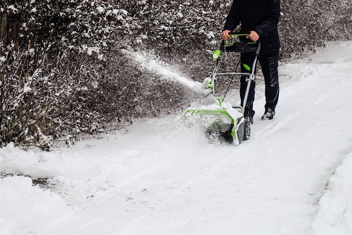 Man using a snow blower to clear the driveway