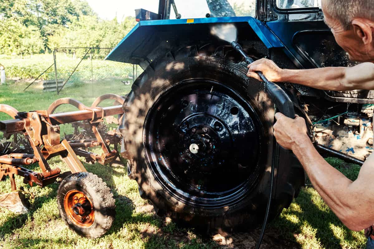 Man washes tractor wheels spraying pressure washer for tractor wash