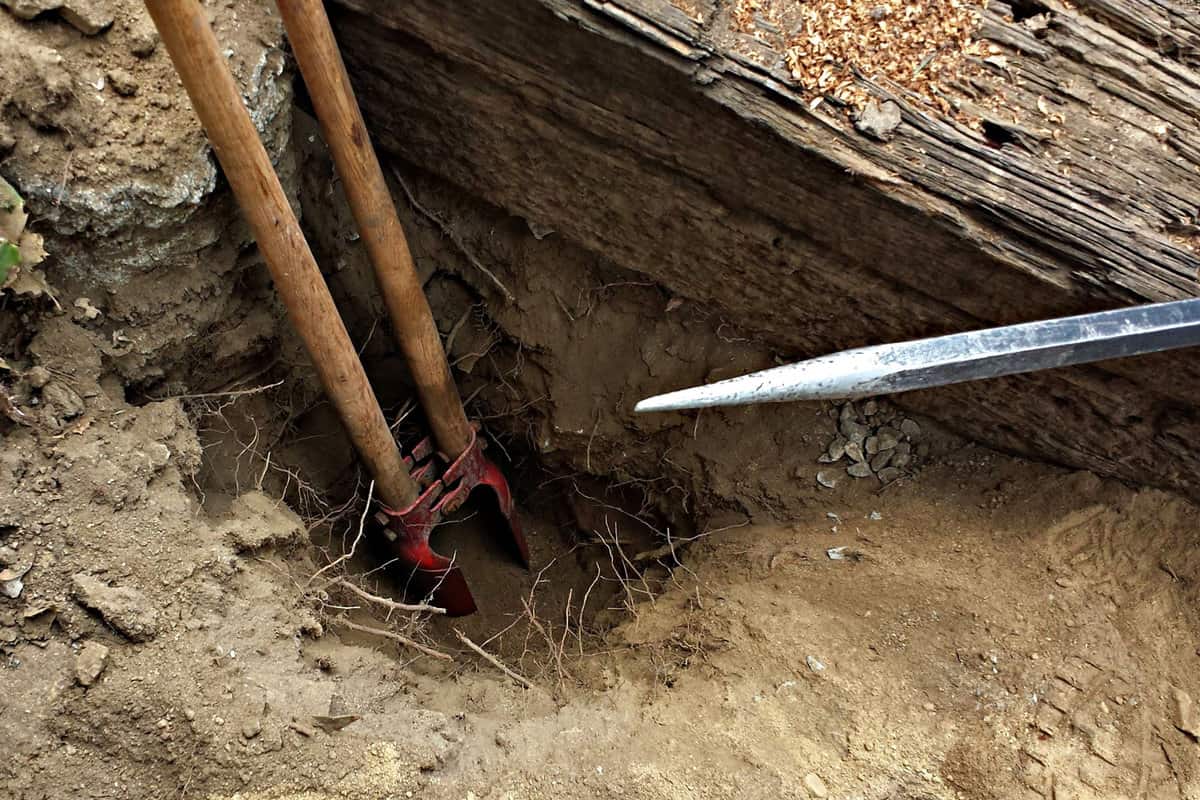 Proper tools such as a posthole digger and a rock bar are being used to dig a fence post hole