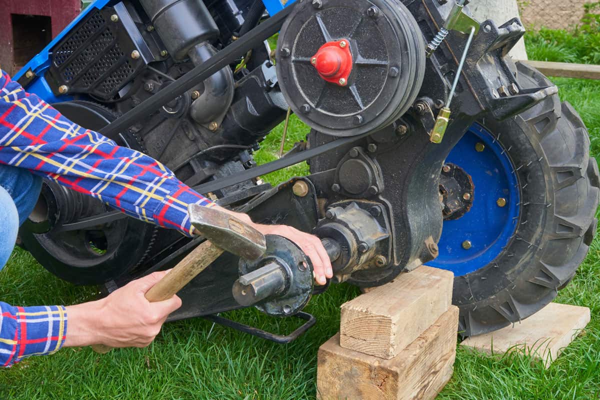 tractor wheel repair,a man knocks out a hammer wedge on the shaft of a two-wheeled tractor
