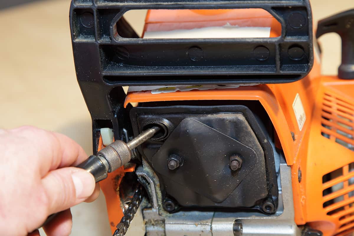 A man's hand cleans the exhaust pipe of a chainsaw muffler