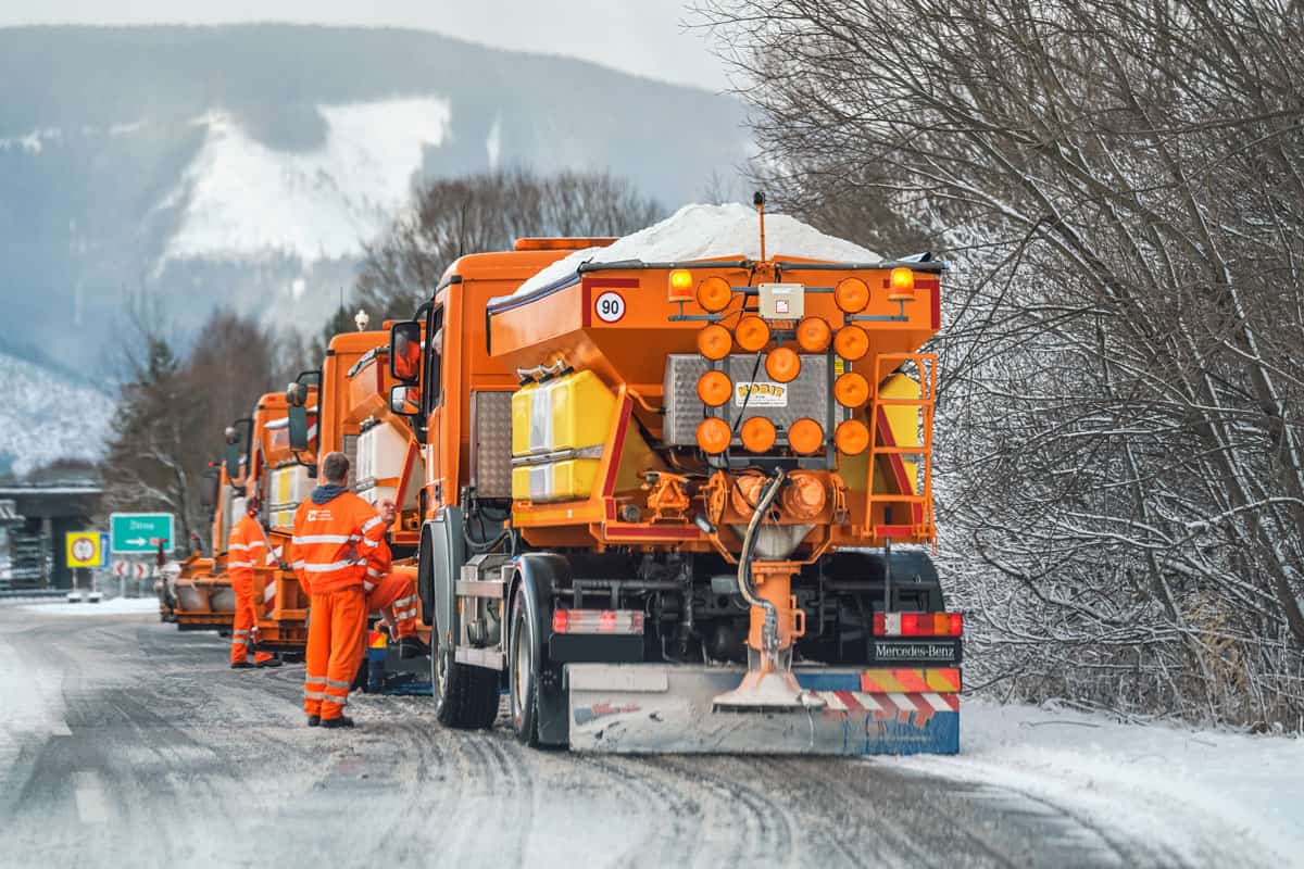 Group of bright orange highway maintenance trucks with de icing salt getting ready on winter
