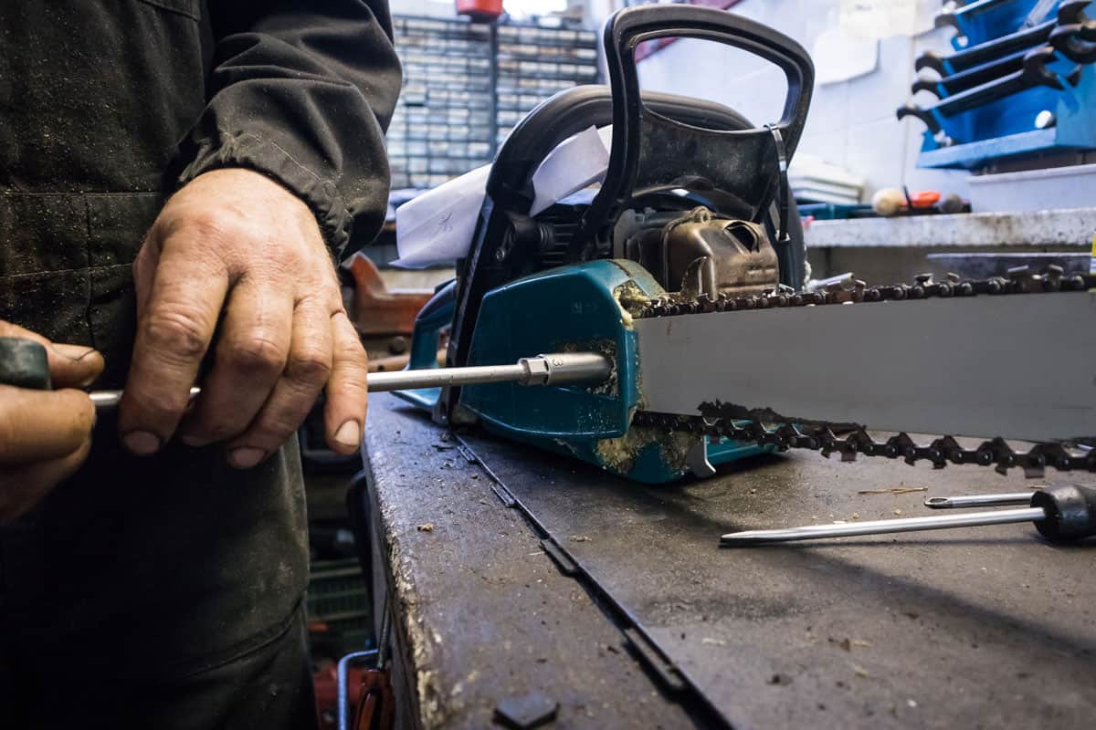 Man is unscrewing the blade of a chainsaw on a work bench in a mechanic shop