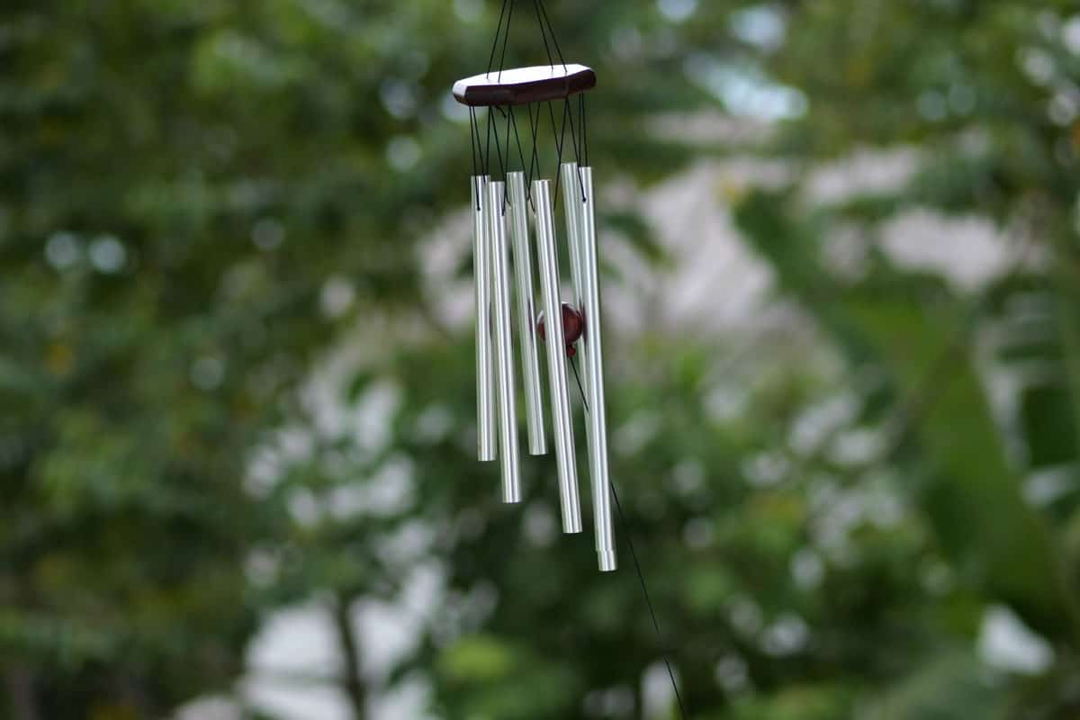 Wind Chimes hangs on the porch of the house against the backdrop of green trees