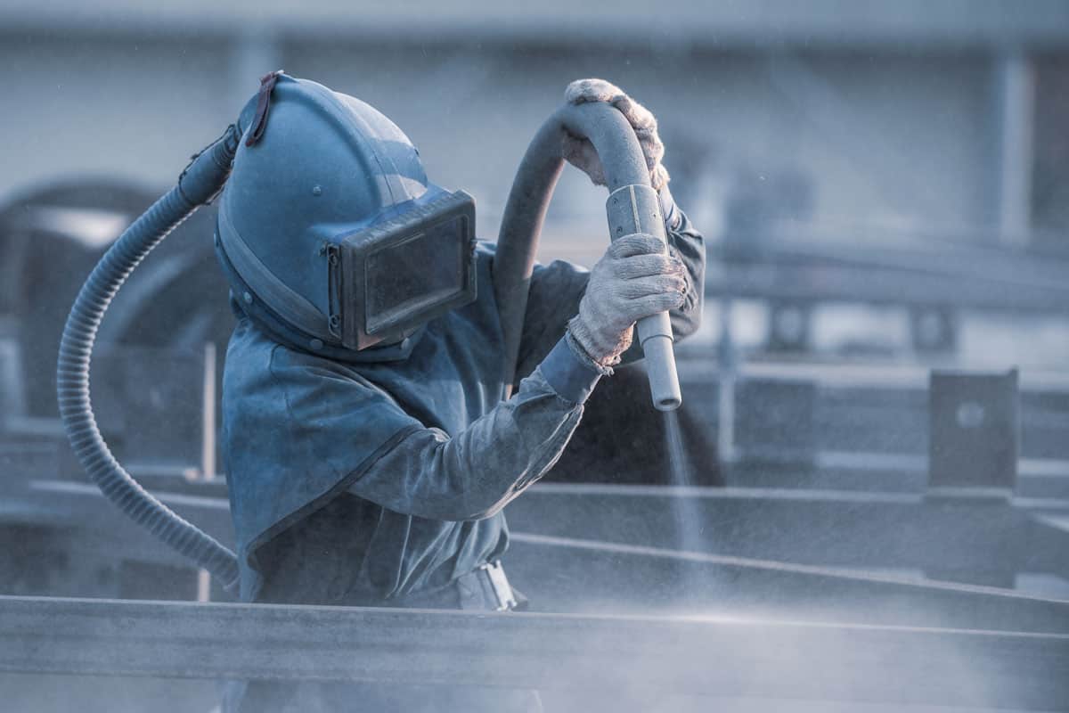 Worker wearing heavy duty protective suit while using a sandblaster