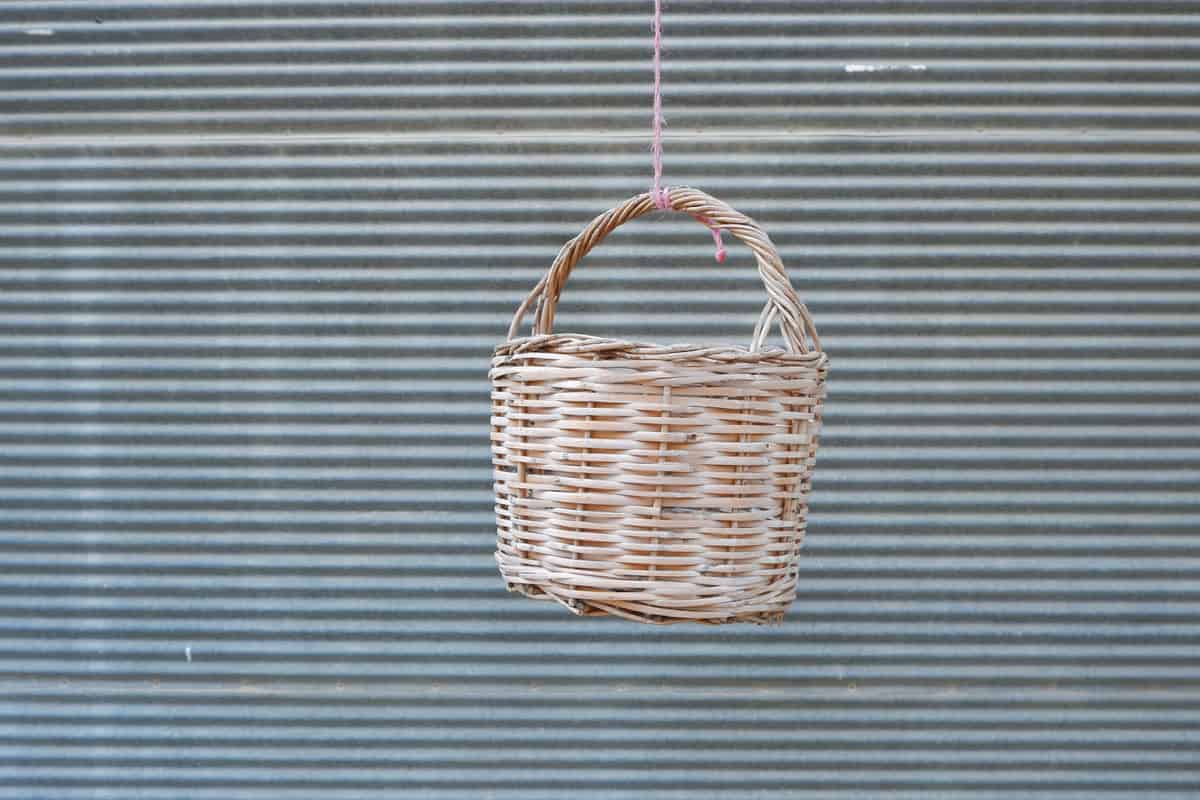 Wicker basket wooden light brown hanging on the rope on the background gray wall 