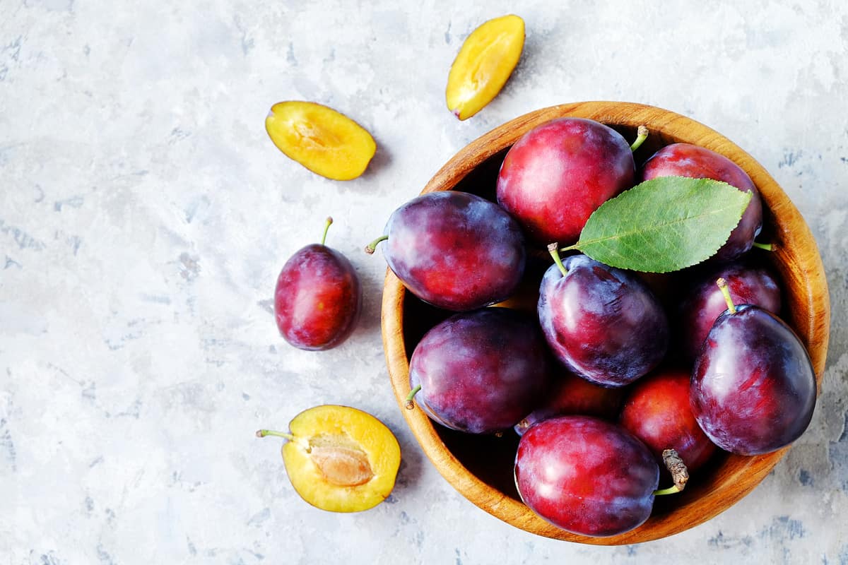 Garden plums in a wooden bowl on textured table.