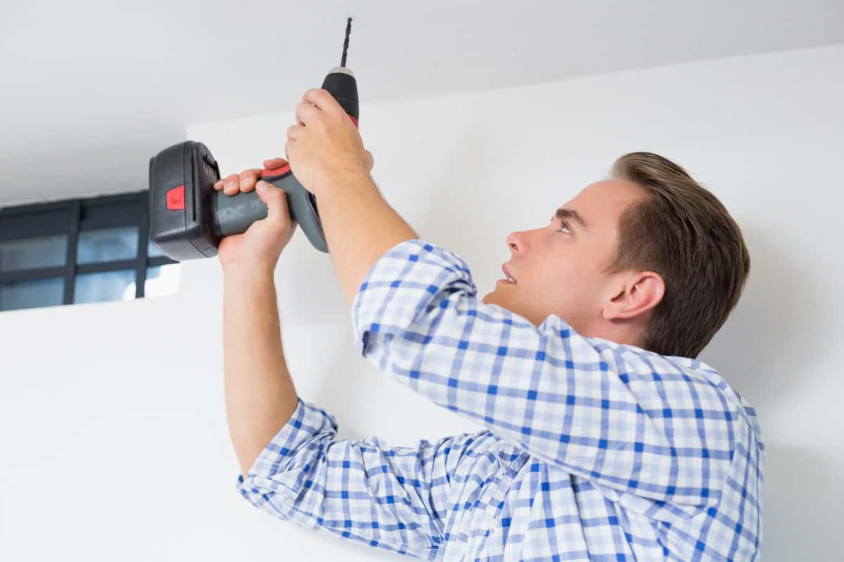 Side view of a young handyman using a cordless drill to the ceiling