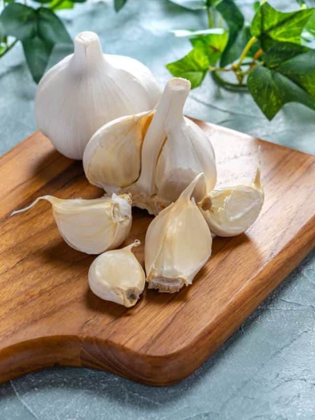 freshly bought garlic bulbs on top of a wood chopping board.
