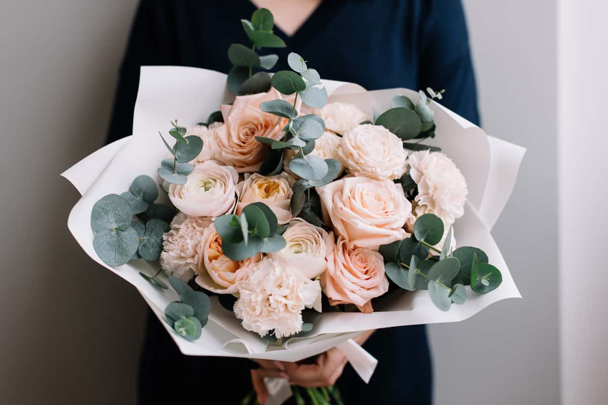 Very nice young woman holding big and beautiful bouquet of fresh roses, carnations, eucalyptus flowers in pastel pink colors