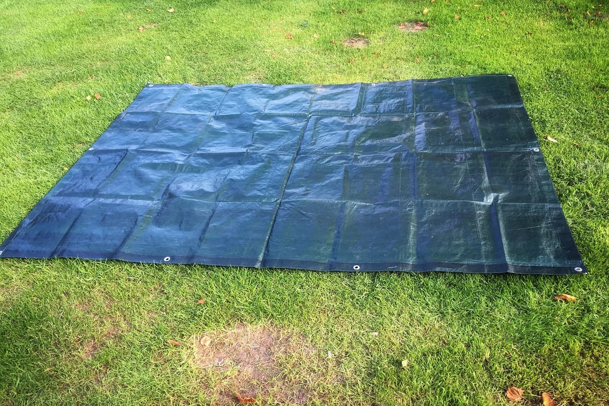 Black tarpaulin tarps spread as ground sheet on grass lawn at campsite
