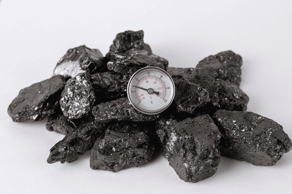 A pile of fossil fuels in the form of coal with a low heat thermometer