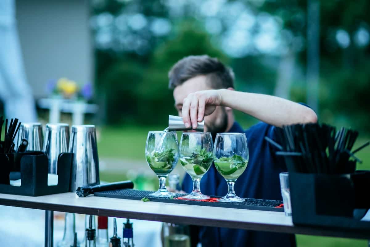 Barman making mojito cocktail and pours alcohol into the glass outdoor
