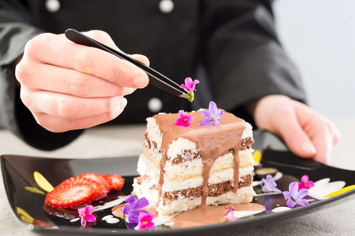 Chef decorate dessert. Decoration of flowers and fruit. Cake with icing.