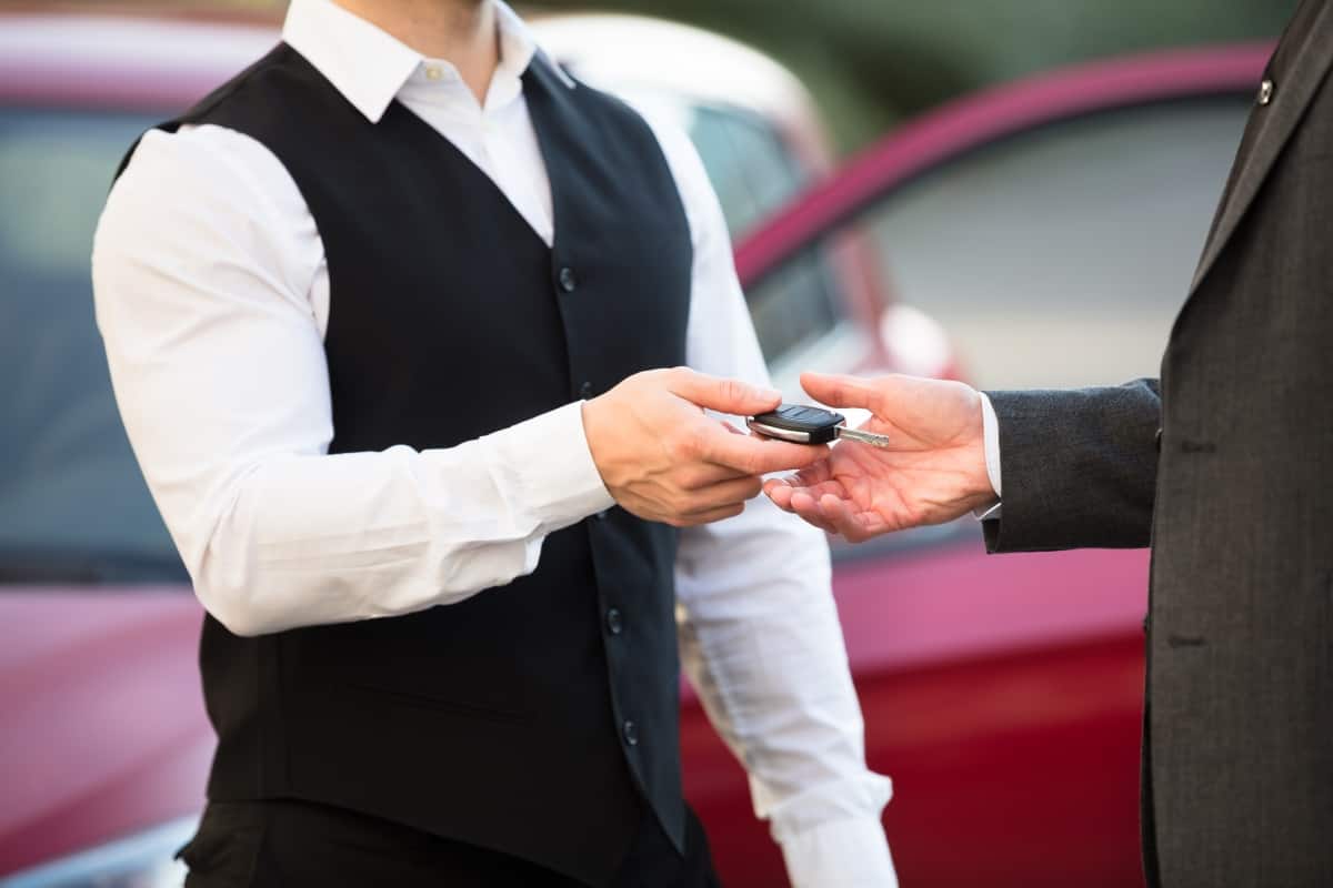 Close-up Of Valet's Hand Giving Car Key To Businessperson