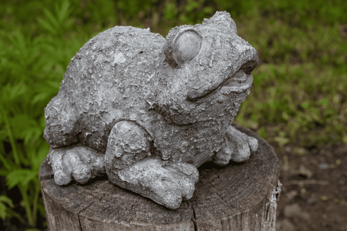 Frog lawn ornament sitting on a cut log