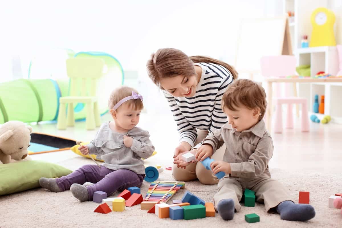 Young nanny playing with little children, indoors