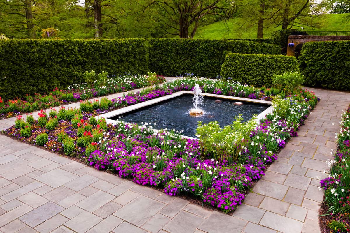A huge and gorgeous garden with a fountain surrounded by flowers
