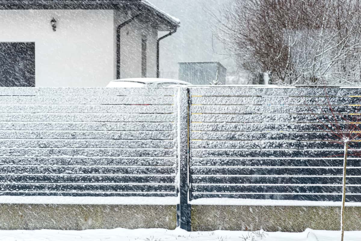 Modern anthracite panel fence with falling smeared snow during a snowstorm