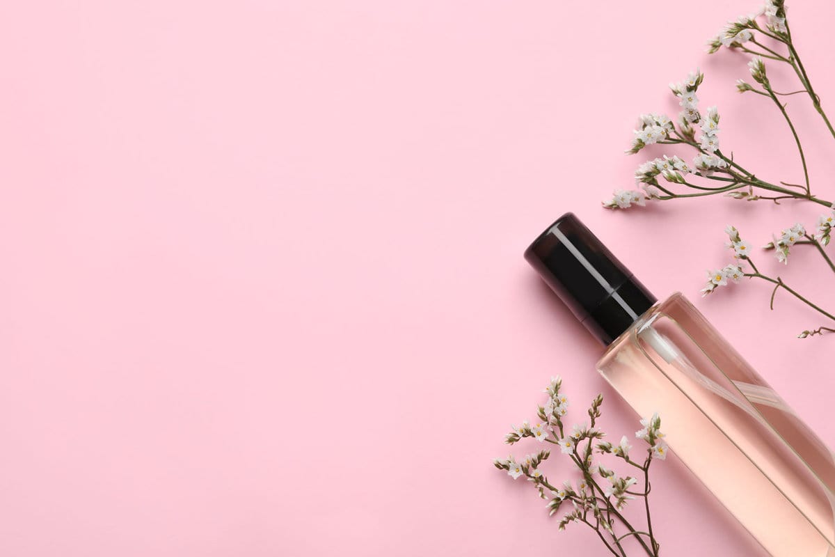 Bottle of baby oil and flowers on pink background, flat lay.