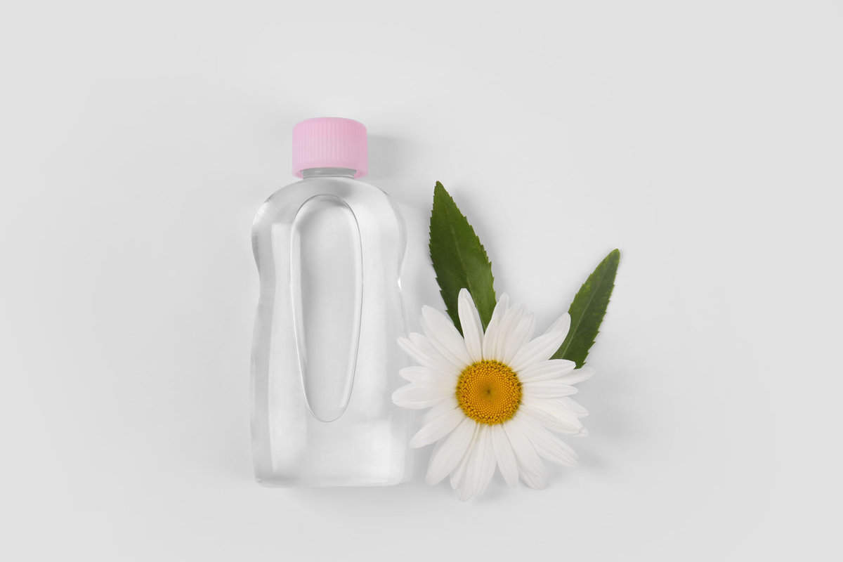 Transparent bottle with baby oil and flower on white background
