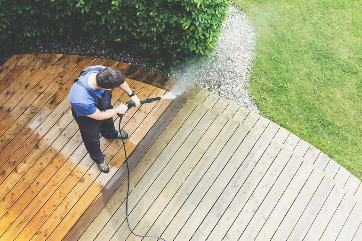 Man using pressure washer to clean the wooden deck