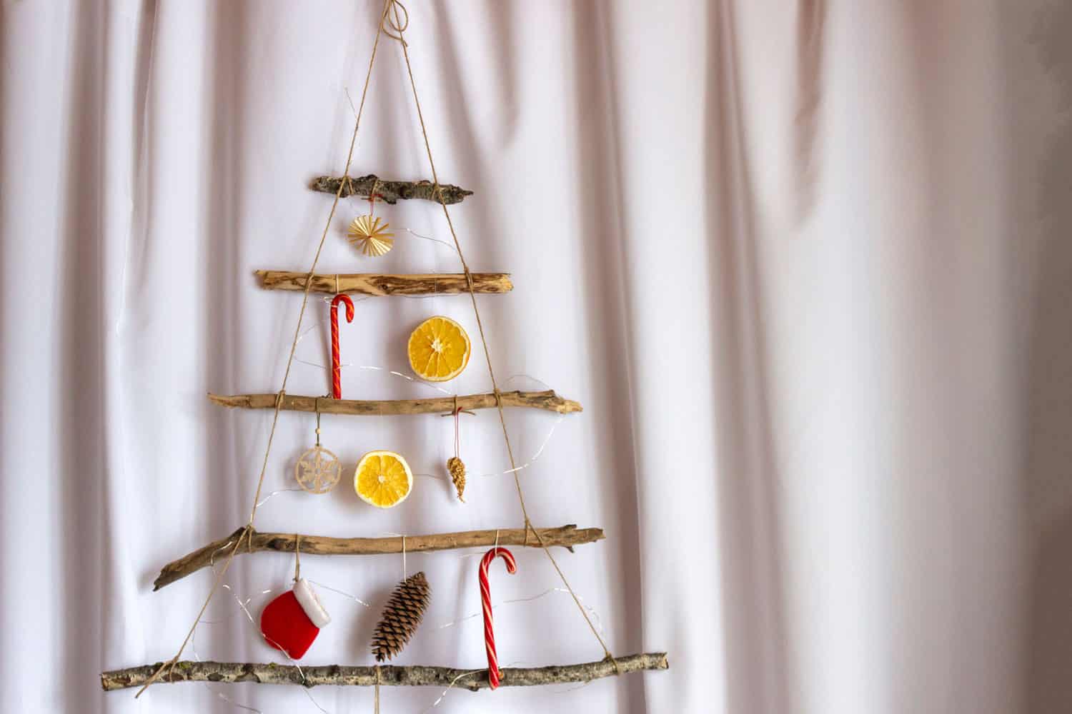 Hand made eco friendly christmas tree out of wooden sticks, oranges, cones and lights