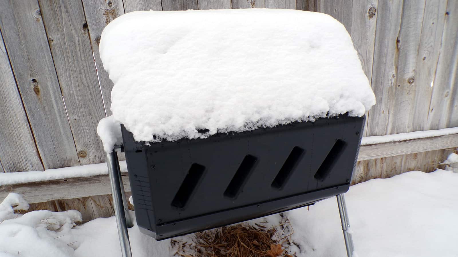A metal composting bin covered in snow
