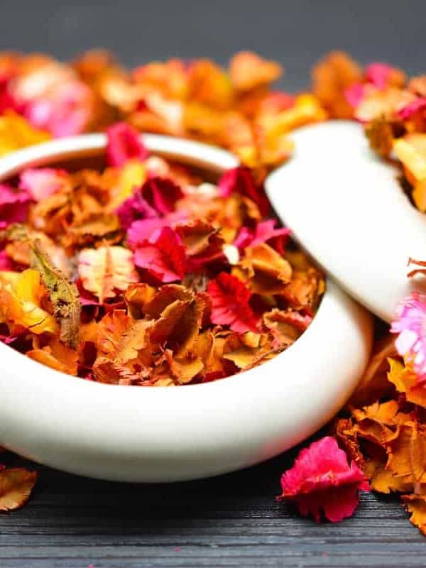 A white ceramic bowl is filled with vividly colored dried flower petals in shades of pink, orange, and yellow, arranged on a dark wooden surface, creating a vibrant contrast --ar 3:4