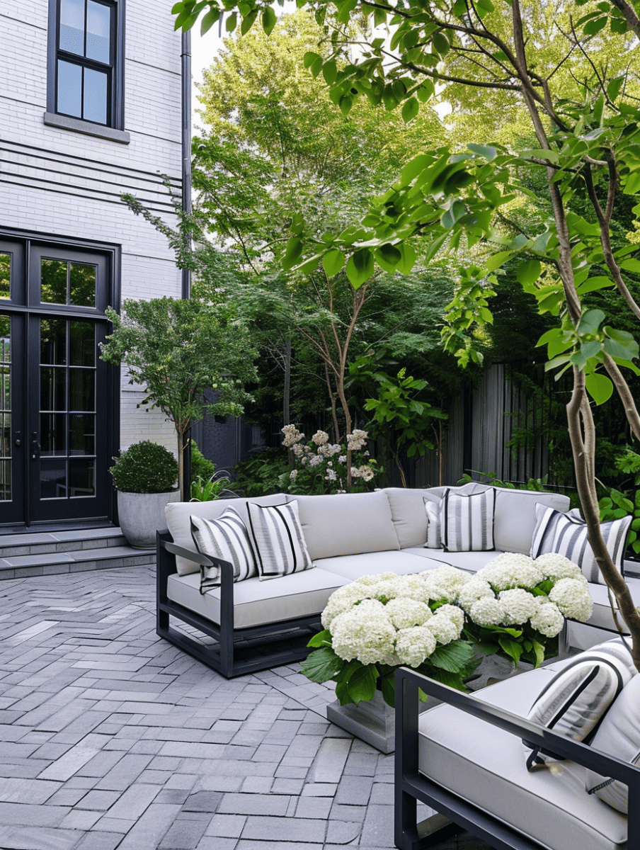 An elegant outdoor seating area with a herringbone patterned brick floor, complemented by a modern sectional sofa with striped pillows, surrounded by lush hydrangeas and greenery, against the backdrop of a white brick home with black framed windows ar 3:4