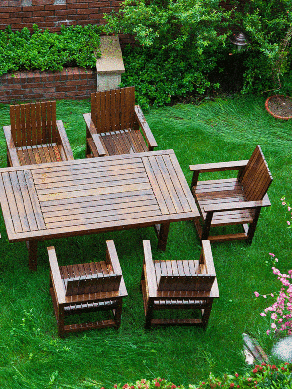 A wooden patio set consisting of a table and six chairs is arranged on a lush green lawn, providing an inviting outdoor dining area adjacent to a brick home with climbing shrubs ar 3:4