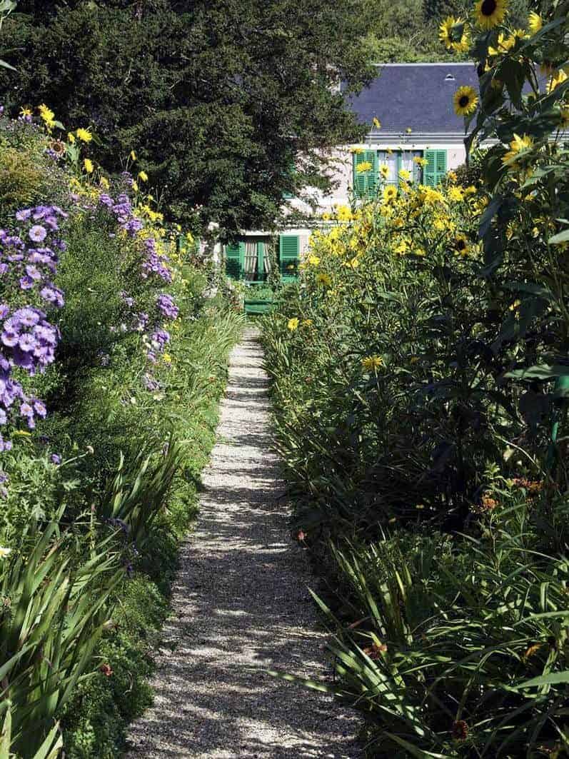 Gravel path leads through a rustic cottage garden to a French country house